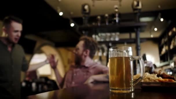 Amigos bebendo cerveja rascunho e assistindo tv em um pub — Vídeo de Stock