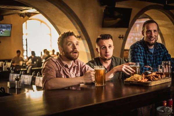 Amigos bebendo cerveja rascunho e assistindo tv em um pub — Fotografia de Stock