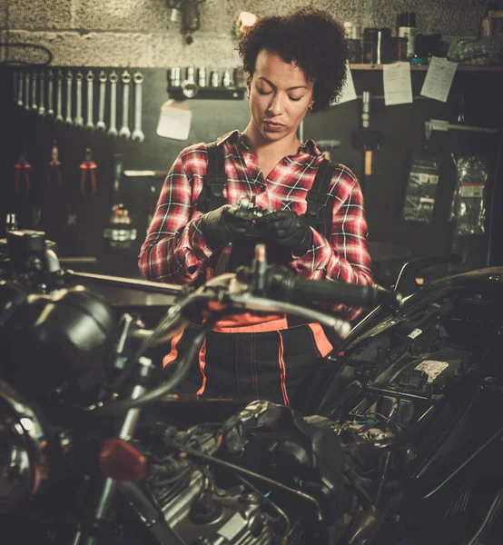 Afrikanisch-amerikanische Mechanikerin repariert ein Motorrad in einer Werkstatt — Stockfoto