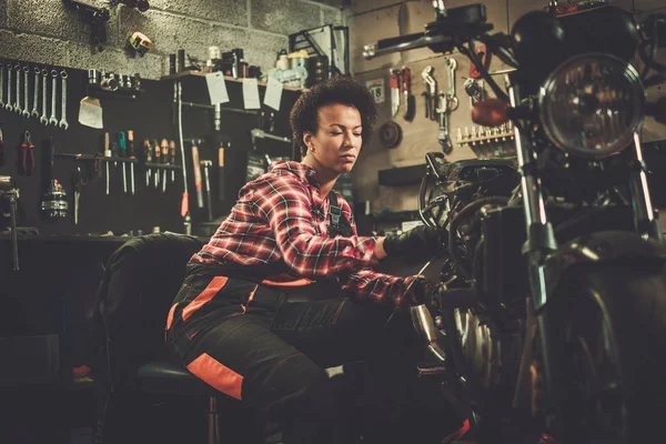 Afrikanisch-amerikanische Mechanikerin repariert ein Motorrad in einer Werkstatt — Stockfoto