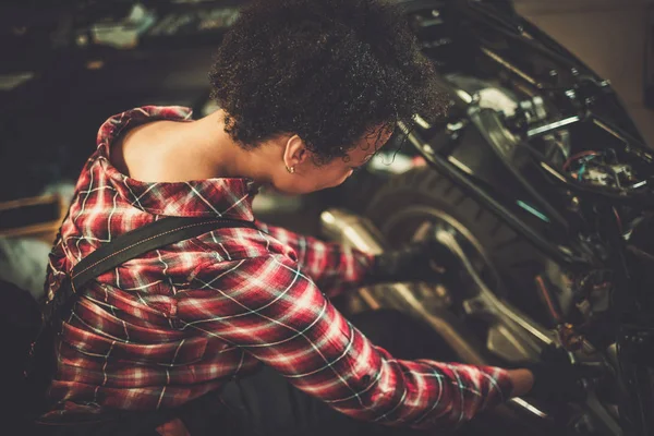 Afrikanisch-amerikanische Mechanikerin repariert ein Motorrad in einer Werkstatt — Stockfoto