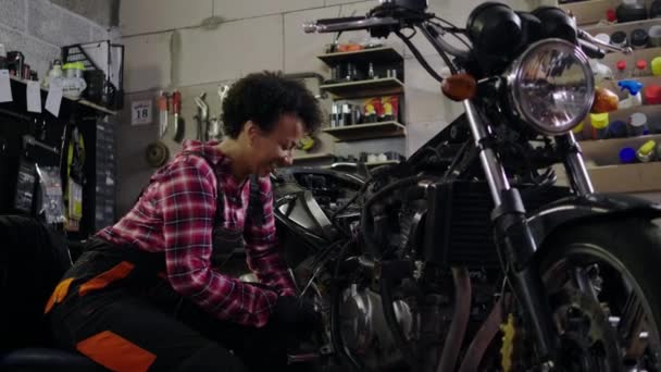 Mujer mecánica afroamericana reparando una motocicleta en un taller — Vídeo de stock