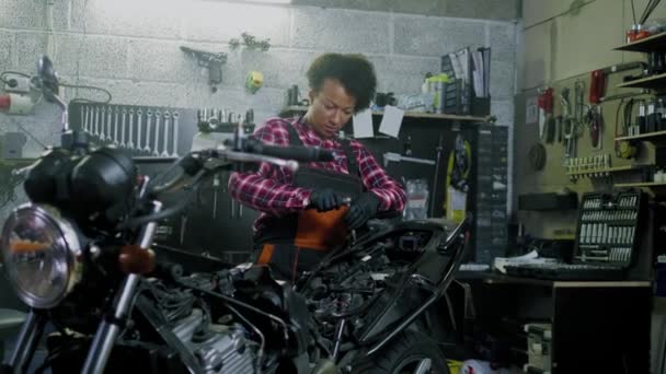 African American vrouw monteur repareren van een motorfiets in een workshop — Stockvideo