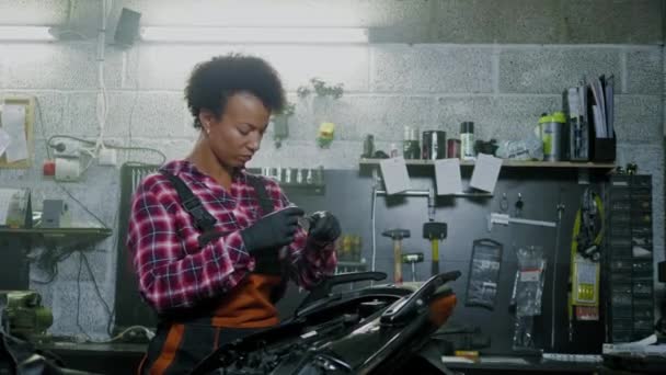 Africano americano mulher mecânico reparando uma motocicleta em uma oficina — Vídeo de Stock