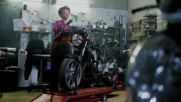 African American vrouw monteur repareren van een motorfiets in een workshop — Stockvideo