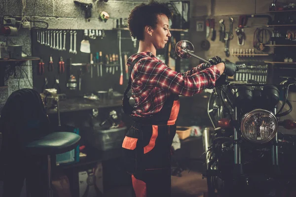 Afrikansk amerikansk kvinna mekaniker reparera en motorcykel i en verkstad — Stockfoto