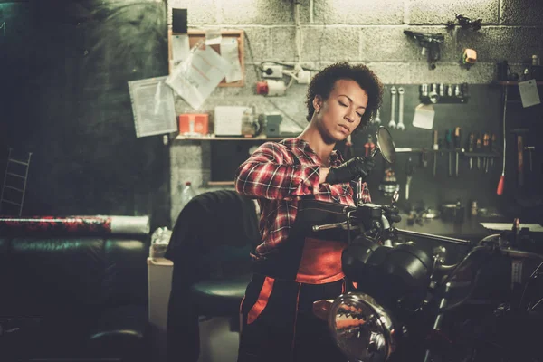 Africano americano mulher mecânico reparando uma motocicleta em uma oficina — Fotografia de Stock