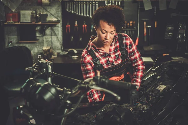 Afrikansk amerikansk kvinna mekaniker reparera en motorcykel i en verkstad — Stockfoto