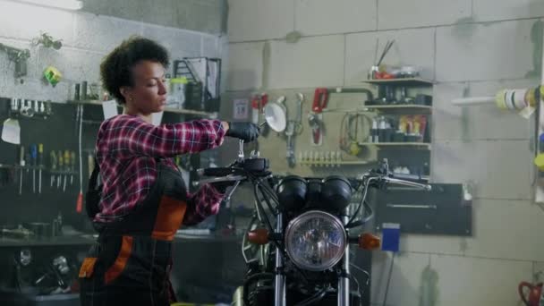 Afrikanisch-amerikanische Mechanikerin repariert ein Motorrad in einer Werkstatt — Stockvideo