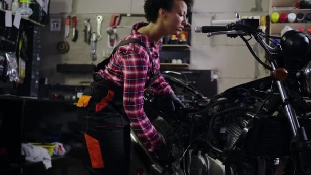 African American vrouw monteur repareren van een motorfiets in een workshop — Stockvideo