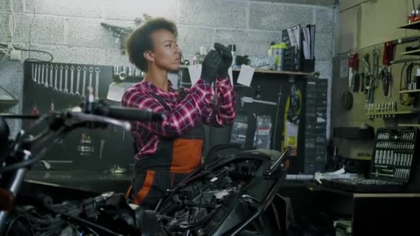Mujer mecánica afroamericana reparando una motocicleta en un taller — Vídeo de stock