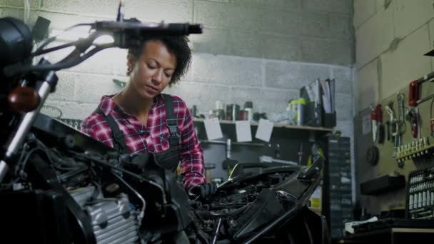 Afrikansk amerikansk kvinna mekaniker reparera en motorcykel i en verkstad — Stockvideo