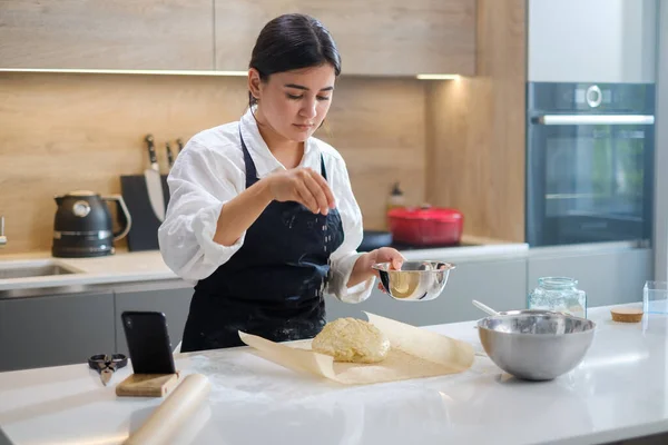 Vrouw chef-kok strooit sesam zaden op haar brood. — Stockfoto