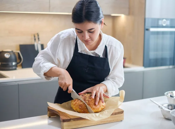 Chica cuidadosamente corta pan recién horneado. — Foto de Stock