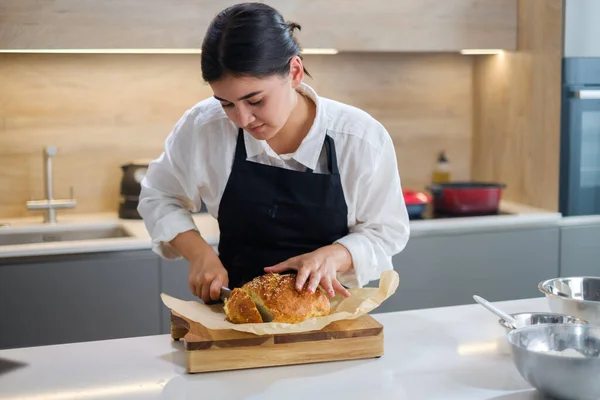 Joven panadero chica cortes su fresco pan. — Foto de Stock