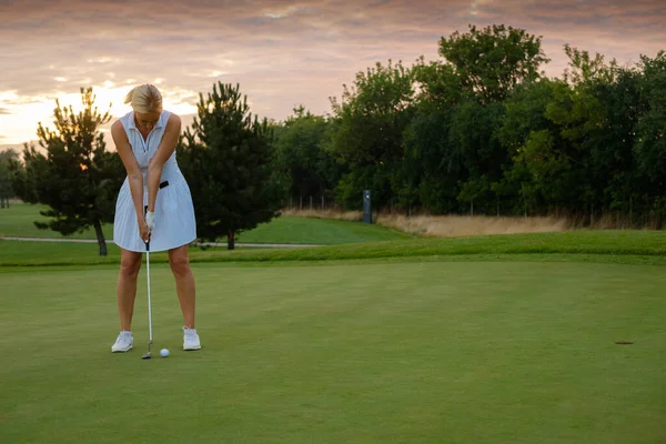 Dama centrada en golpear la bola en el agujero del golf . — Foto de Stock