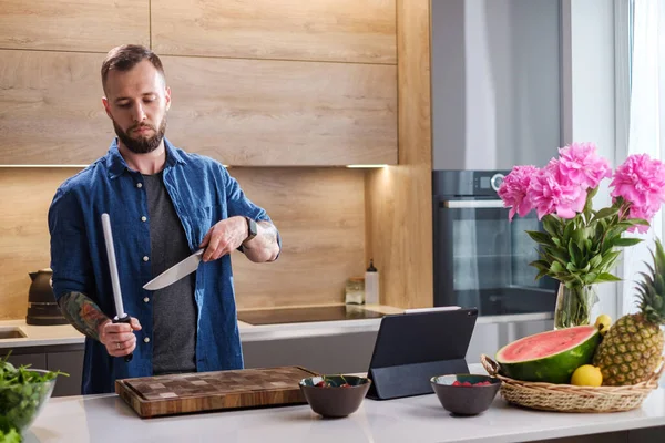 Serieuze man slijpen mes voor het snijden van groenten . — Stockfoto