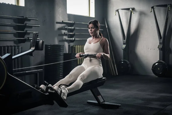 Mujer de uniforme tiene entrenamiento en máquina de remo . — Foto de Stock