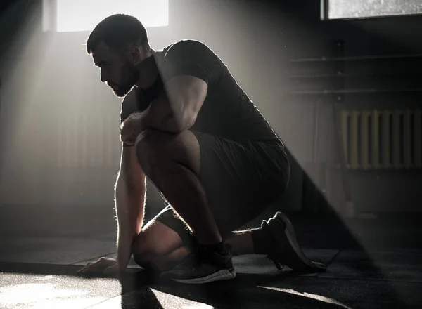 Hombre deportivo sentarse en el gimnasio oscuro . — Foto de Stock