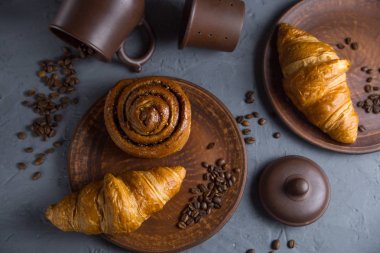 klasik Fransız kruvasan, gri bir arka plan üzerinde pişmiş ürünler kahve çekirdekleri ile çevrili bir işçilik çanak yatıyor