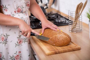 Kadın mutfaktaki tahtada metal bir bıçakla güzel kokulu ekmek kesiyor.