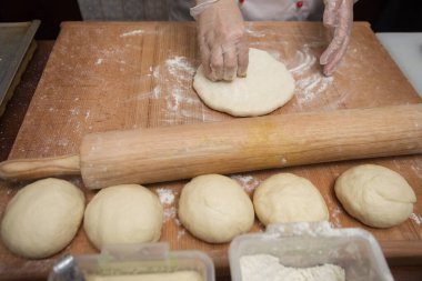 Aşçı masada merdaneyle hamuru yuvarlıyor.