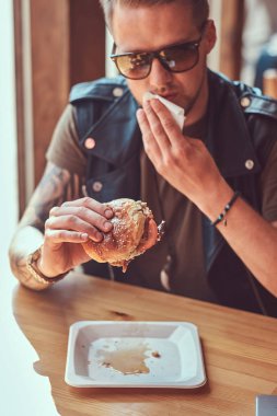 Bir hamburger yeme bir şık saç ve sakal ile yakışıklı hipster yol kenarına yerleştirilen bir kafede yemek yemeye karar verdim bir masada oturur.
