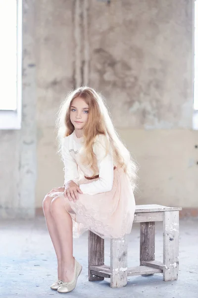 Charming little girl model sitting in a wooden chair in a studio. — Stock Photo, Image