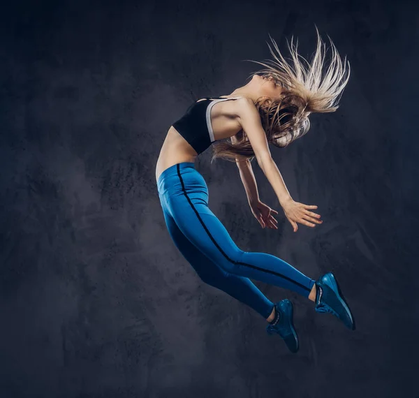 Jovem bailarina loira em danças de sportswear e salta em um estúdio. Isolado em um fundo escuro . — Fotografia de Stock