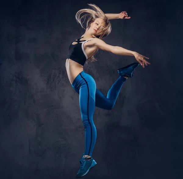 Молода блондинка балерина в спортивному одязі танцює і стрибає в студії. Ізольовані на темному тлі . — стокове фото