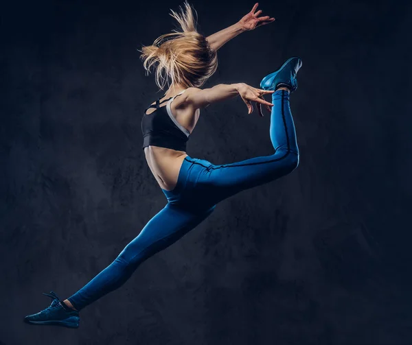 Mladá blondýna baletka v sportovní tance a skoky ve studiu. Na tmavém pozadí, samostatný. — Stock fotografie