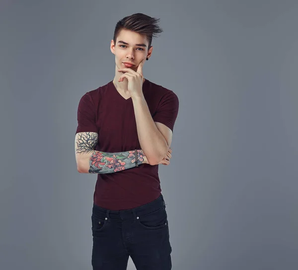 Csinos, divatos fiatal srác elegáns haj és a tetoválás a karján pózol egy stúdió. — Stock Fotó