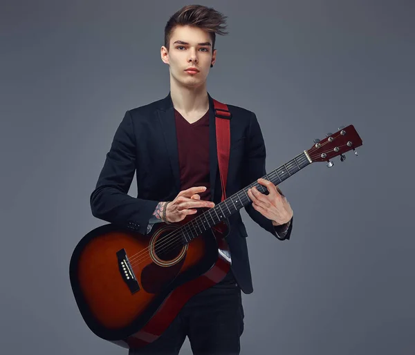 Yakışıklı genç müzisyen bir akustik gitar çalmaya şık giysiler içinde şık saç ile. — Stok fotoğraf