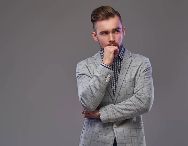 Hombre elegante guapo pensativo en una chaqueta gris elegante, posando con la mano en la barbilla . — Foto de Stock