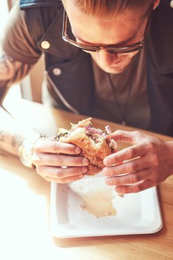 Bir şık saç ve sakal aç hipster adamla portresi bir hamburger yeme yol kenarına yerleştirilen bir kafede yemek yemeye karar verdim bir masada oturur.