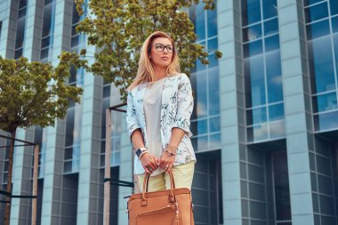 Şık giysiler ve gözlük bir gökdelen karşı duran bir çanta ile güzel moda kadın.