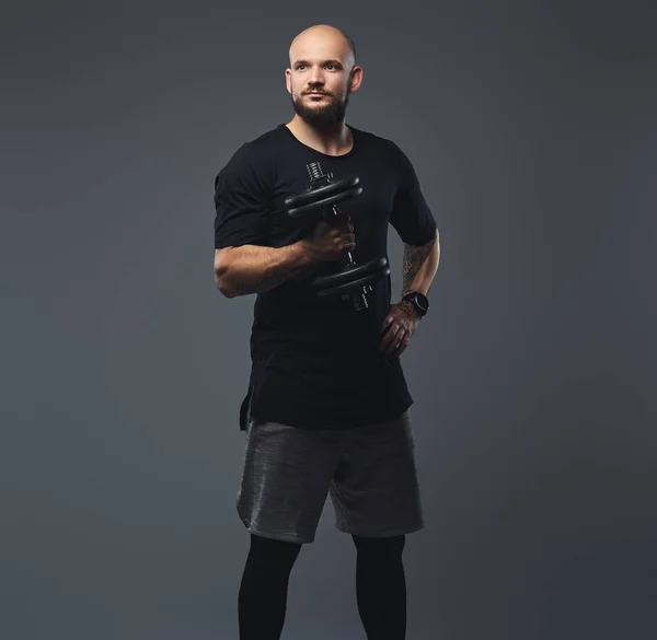 Portret van een knappe bebaarde atleet in een zwart t-shirt, poseren halter in een studio. — Stockfoto