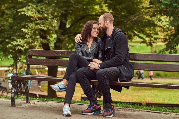 Aantrekkelijke moderne paar zittend op een bank in een park. — Stockfoto