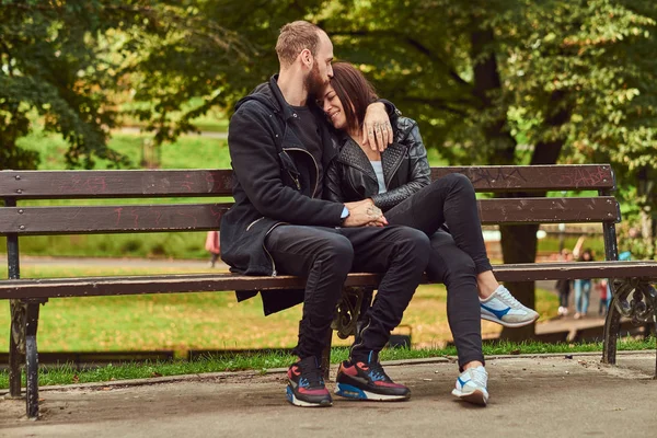 Ελκυστικό μοντέρνο ζευγάρι κάθεται σε ένα παγκάκι στο πάρκο. — Φωτογραφία Αρχείου