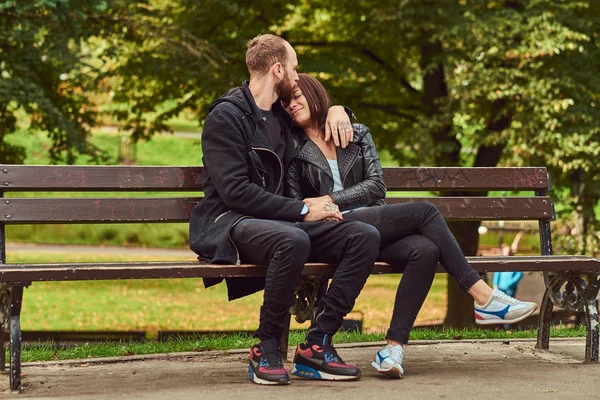 Ελκυστικό μοντέρνο ζευγάρι κάθεται σε ένα παγκάκι στο πάρκο. — Φωτογραφία Αρχείου