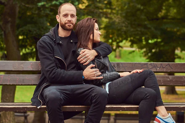 Atractiva pareja moderna sentada en un banco en un parque . —  Fotos de Stock