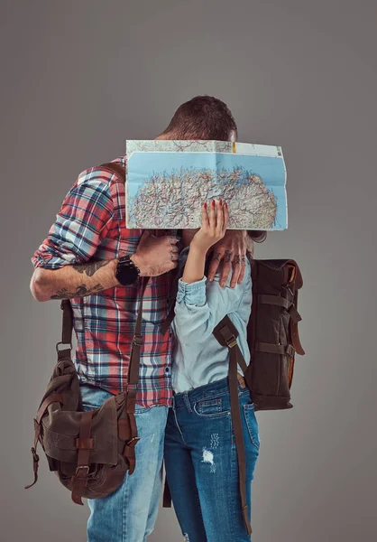 Casal atraente de turistas beijando enquanto cobria seu rosto com um mapa, abraçando em um estúdio . — Fotografia de Stock