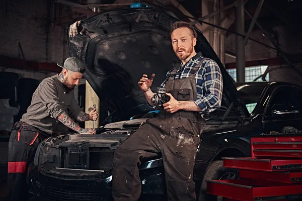 Dwóch brodatych auto mechanik w jednolite, naprawić uszkodzony samochód w garażu. — Zdjęcie stockowe