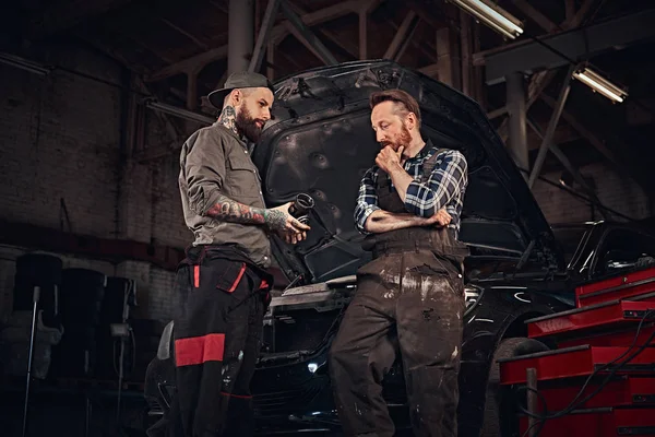 Deux mécaniciens parlent pendant les réparations d'une voiture cassée dans un garage . — Photo