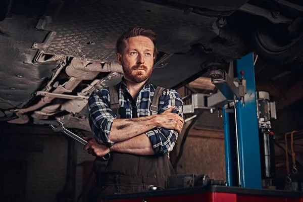Mecánico cruzó las manos mientras estaba de pie debajo de levantar el coche en un garaje de reparación . —  Fotos de Stock