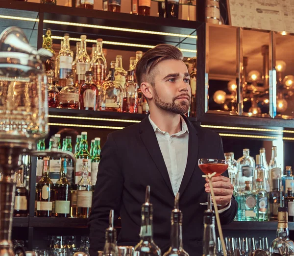 Красивый стильный мужчина держит стакан эксклюзивного алкоголя на заднем плане барной стойки . — стоковое фото
