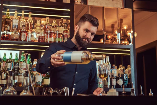 Elegante brutal barman no preto camisa faz um coquetel no bar contador de fundo . — Fotografia de Stock