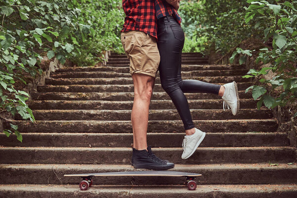 Cropped image of young hipster couple, cuddling while standing on steps in a park.