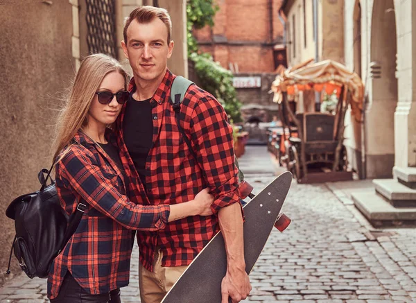 Молодая пара хипстеров, красивый фигурист и его девушка обнимаются, стоя на старой улице Европы . — стоковое фото