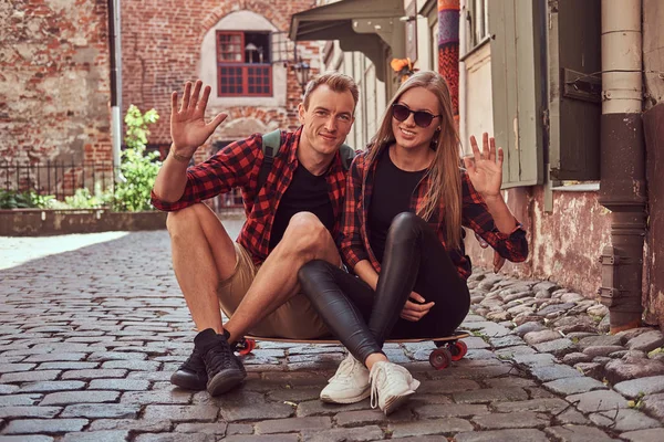 Молодая счастливая пара хипстеров, отдых во время прогулки сидя на тротуаре на старой улице Европы . — стоковое фото